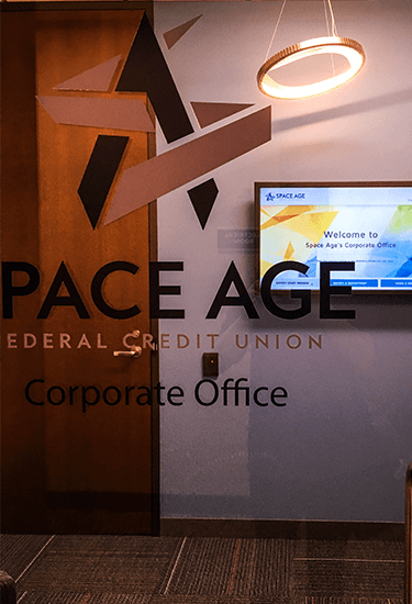 A window with "Space Age Federal Credit Union" and a welcome signage screen in the background