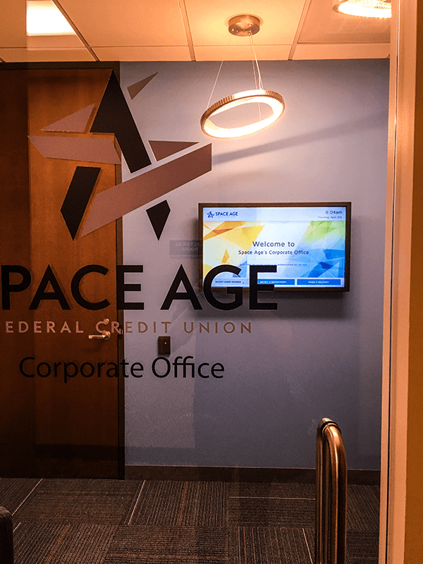 A window with "Space Age Federal Credit Union" and a welcome signage screen in the background