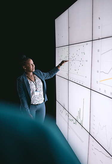 A business woman giving a presentation as she points her finger towards data on a video wall