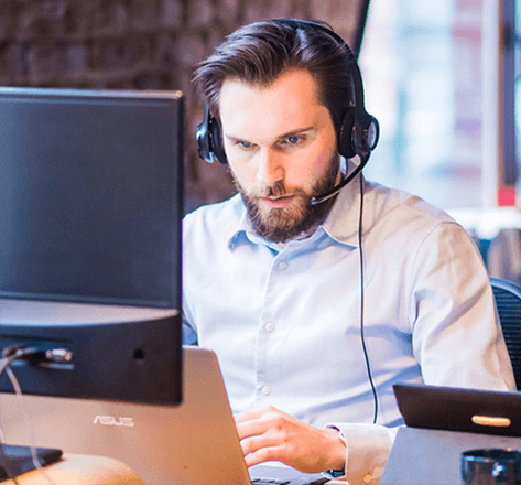 man with headphones sitting at a desk, using a laptop