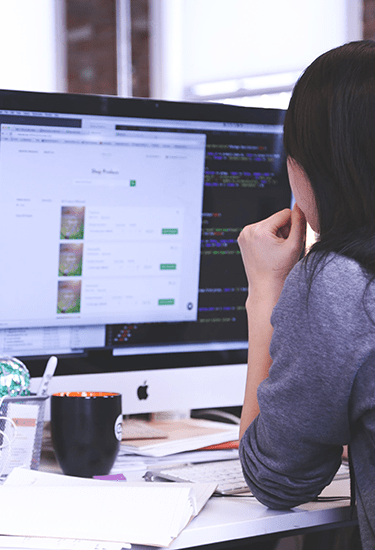 a woman coding a program on a mac with paper and notebooks on the desk